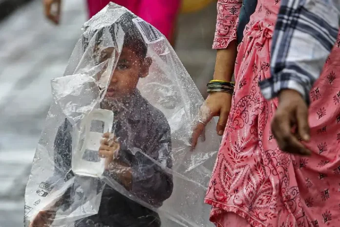 A child takes cover under a plastic sheet during rain. PTI/The Telegraph